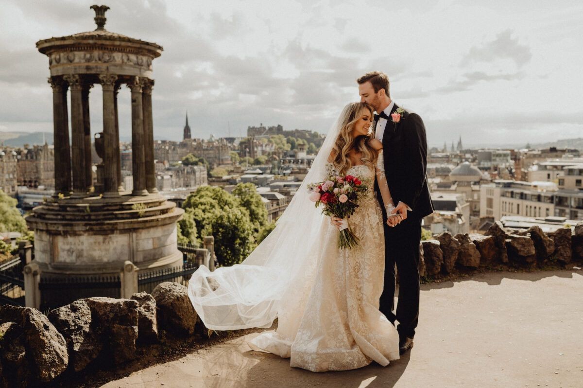 Bride and groom pose in front of a historic monument overlooking a city skyline.